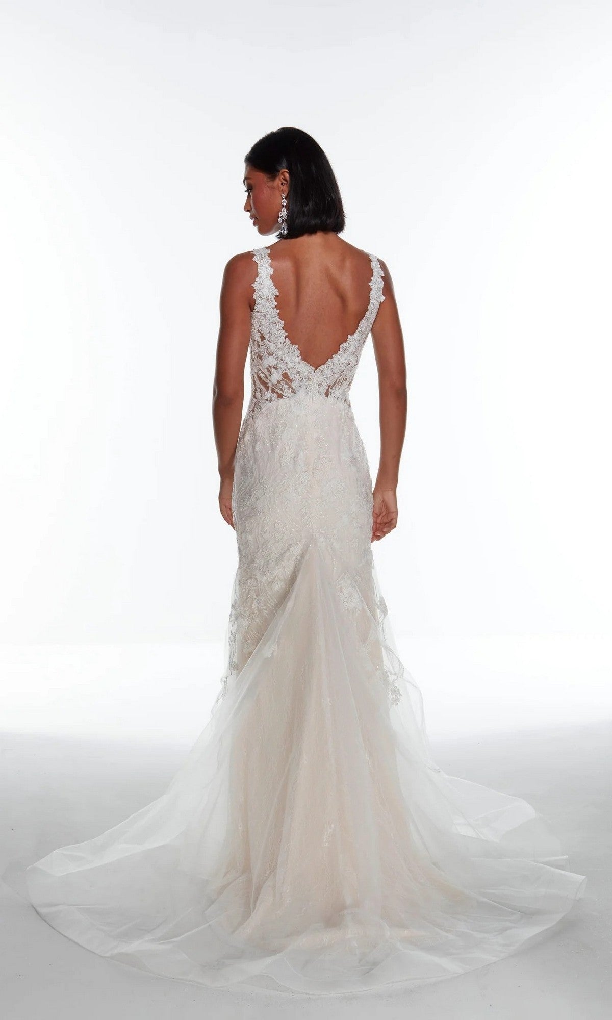 A woman faces away in the Long White Dress: Alyce 7017, featuring a backless design, trumpet skirt, and long lace train, set against a plain white background.